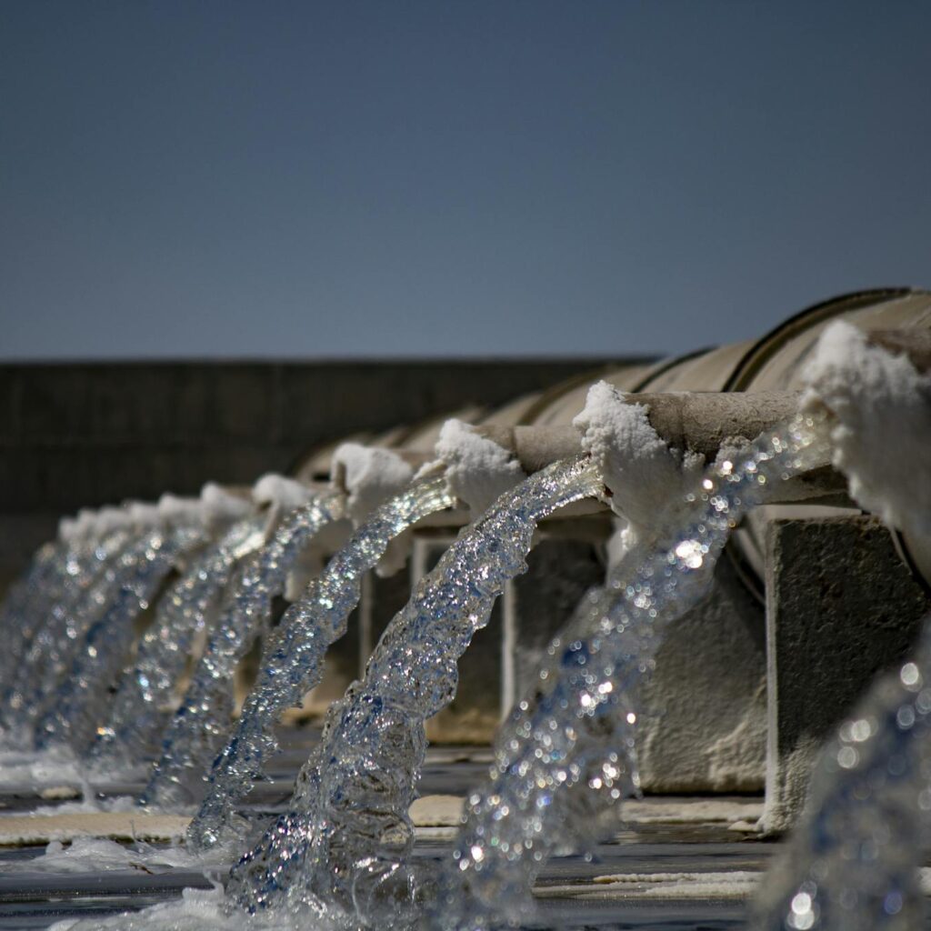 Close-up view of water flowing from industrial pipes against a clear blue sky.